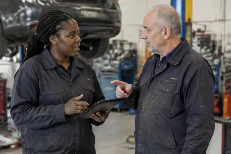 Two experienced colleagues discussing a tablet in a vehicle workshop
